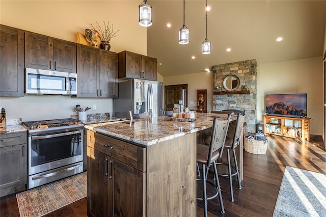 kitchen featuring decorative light fixtures, stainless steel appliances, a kitchen island with sink, a breakfast bar area, and dark wood-type flooring