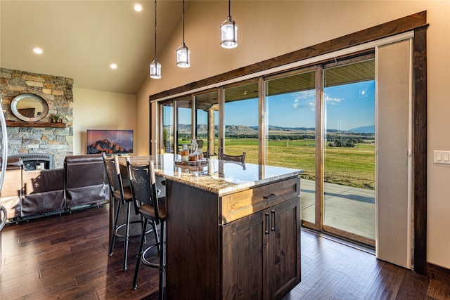 kitchen with decorative light fixtures, dark hardwood / wood-style flooring, a stone fireplace, and a kitchen island with sink