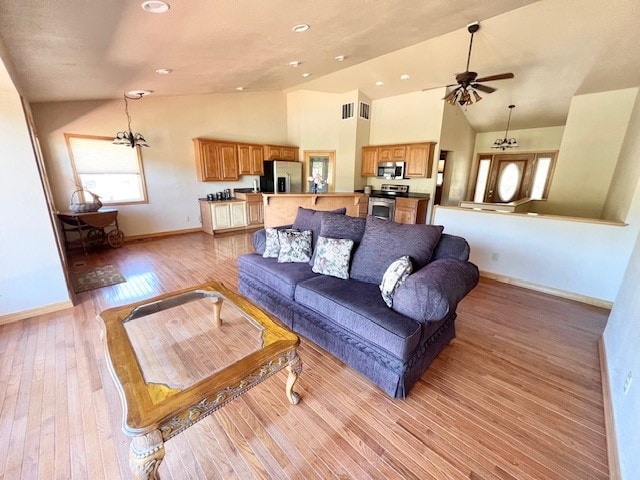 living room with high vaulted ceiling, light wood-type flooring, and ceiling fan with notable chandelier