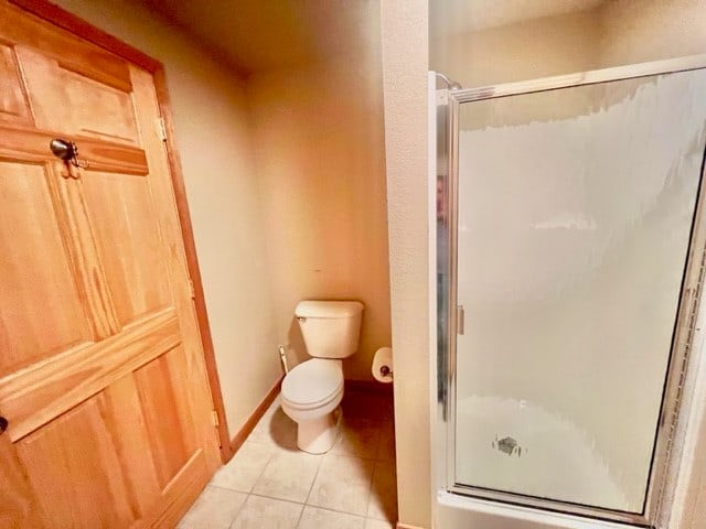 bathroom featuring tile flooring, toilet, and a shower with door