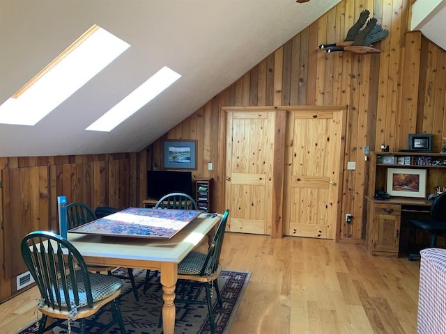 dining space with vaulted ceiling with skylight, wood walls, and light wood-type flooring