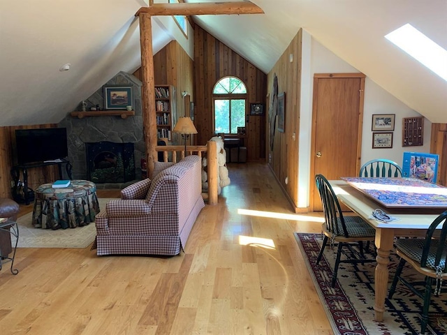 living room featuring vaulted ceiling with beams, light hardwood / wood-style floors, a stone fireplace, and wooden walls