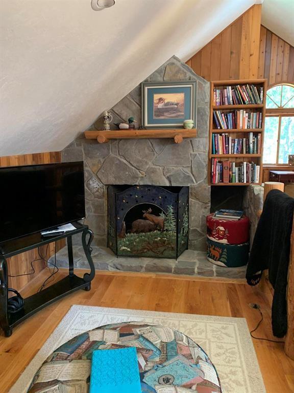 living area with a fireplace, wood-type flooring, lofted ceiling, and wood walls