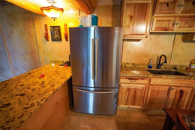 kitchen with stainless steel fridge, wood walls, sink, dark tile floors, and light stone countertops