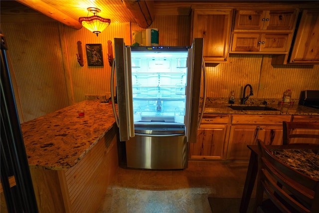 kitchen featuring stainless steel refrigerator, tile flooring, wooden walls, stone countertops, and sink