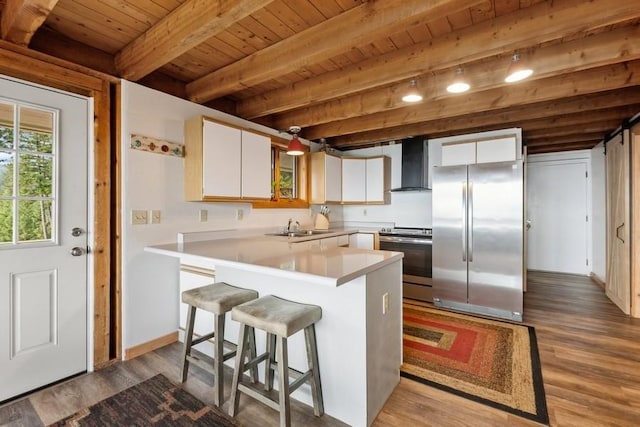 kitchen featuring stainless steel appliances, light countertops, white cabinetry, a sink, and wall chimney exhaust hood