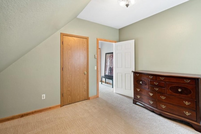 unfurnished bedroom with light carpet, baseboards, vaulted ceiling, and a textured ceiling