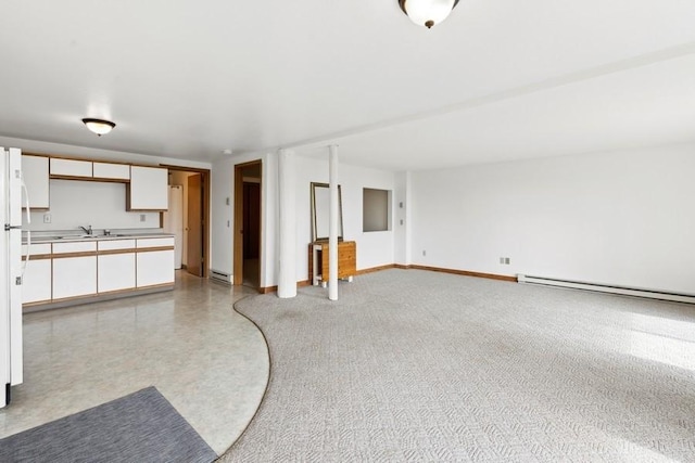 unfurnished living room with baseboard heating, a sink, and baseboards