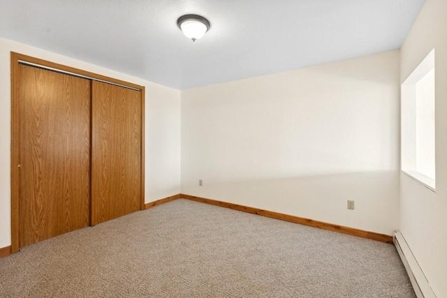 unfurnished bedroom with a baseboard heating unit, a closet, light colored carpet, and baseboards