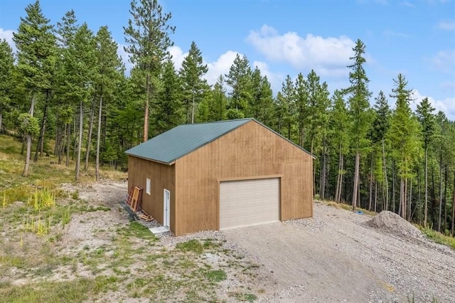 detached garage with gravel driveway and a view of trees