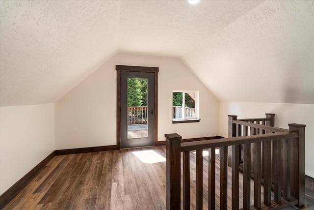 bonus room with dark wood-type flooring, vaulted ceiling, and a textured ceiling