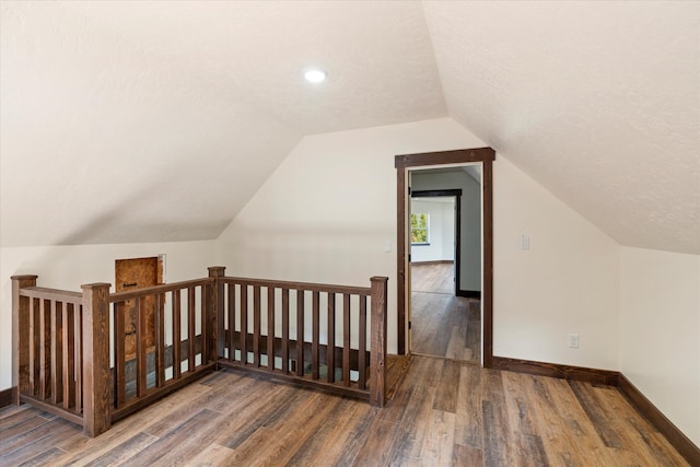 additional living space with dark hardwood / wood-style flooring, a textured ceiling, and vaulted ceiling