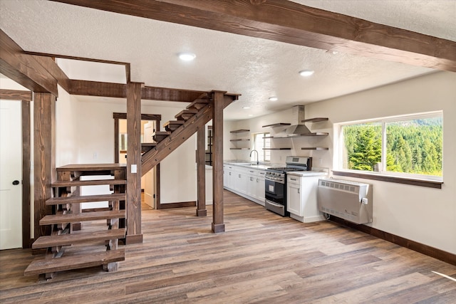 kitchen featuring light hardwood / wood-style floors, a textured ceiling, white cabinetry, wall chimney exhaust hood, and stainless steel gas range oven