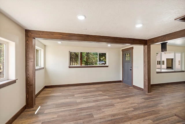 empty room featuring beamed ceiling, a healthy amount of sunlight, a textured ceiling, and dark hardwood / wood-style flooring