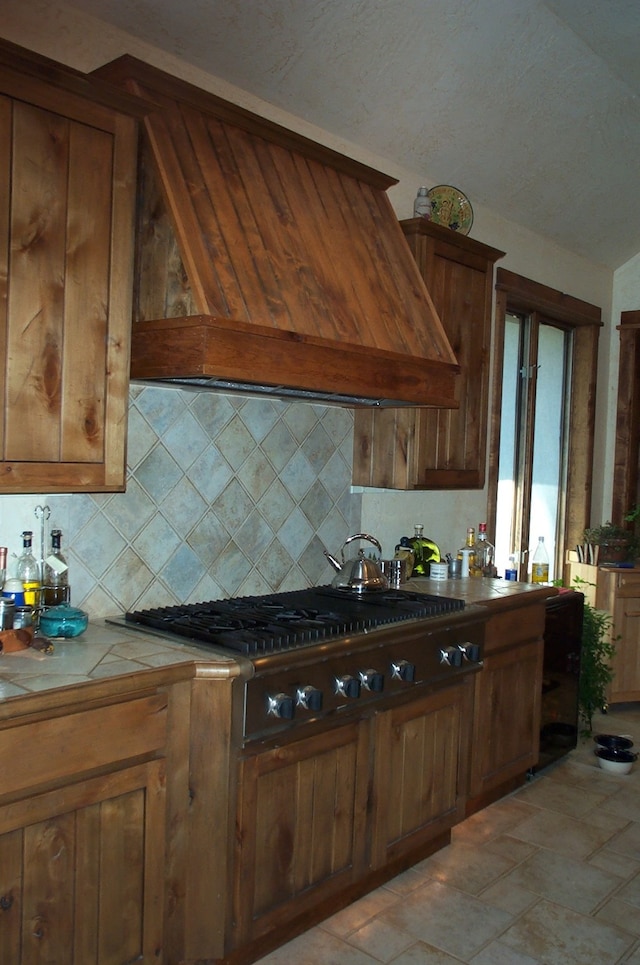 kitchen featuring stainless steel gas stovetop, light tile patterned floors, premium range hood, tile counters, and backsplash