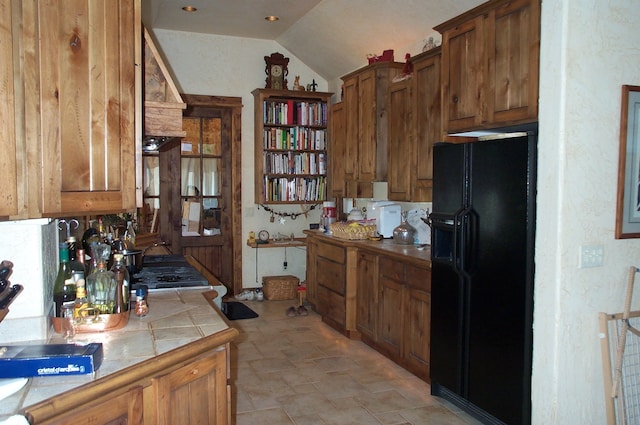 kitchen with black fridge with ice dispenser, tile counters, light tile patterned floors, and lofted ceiling