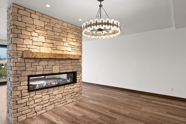 unfurnished living room featuring a notable chandelier, recessed lighting, a stone fireplace, wood finished floors, and baseboards