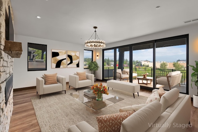 living area with a notable chandelier, visible vents, a stone fireplace, wood finished floors, and baseboards