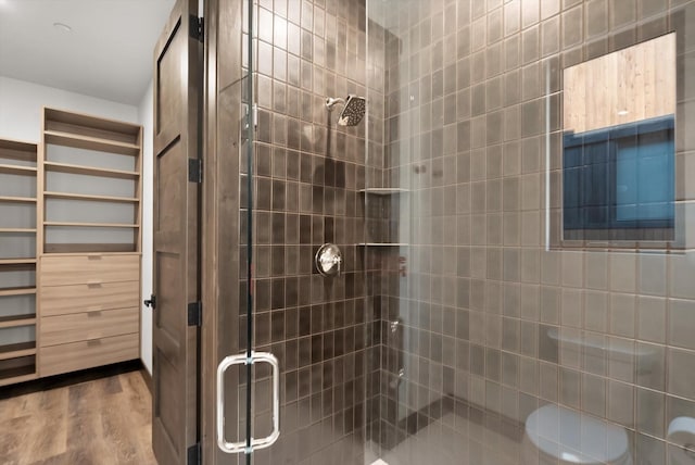 bathroom with tiled shower, wood finished floors, and toilet