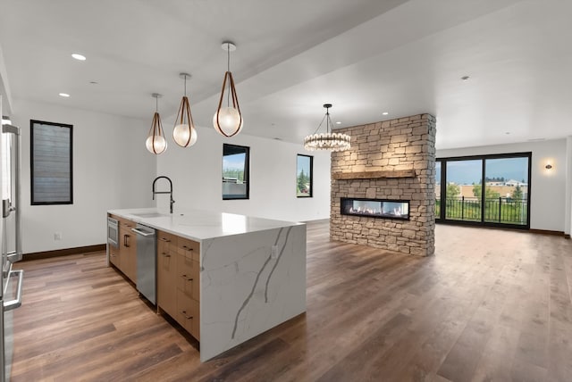 kitchen with open floor plan, hanging light fixtures, a center island with sink, and light stone countertops