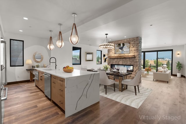 kitchen with dishwasher, open floor plan, hanging light fixtures, a kitchen island with sink, and a sink