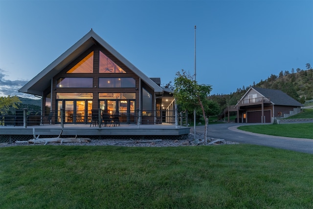 back house at dusk with a wooden deck and a lawn