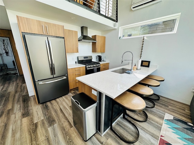 kitchen with a kitchen bar, stainless steel appliances, dark wood-type flooring, and wall chimney exhaust hood