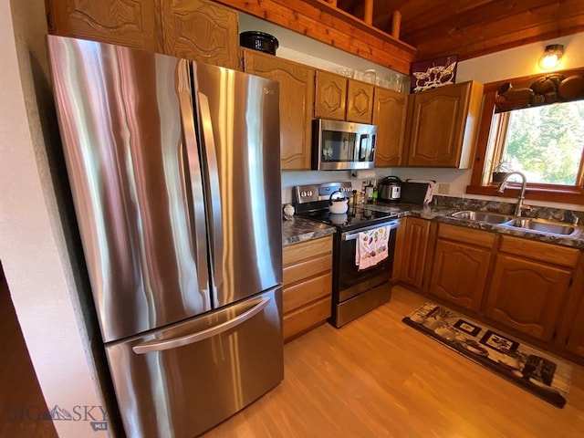 kitchen with dark stone countertops, light hardwood / wood-style flooring, appliances with stainless steel finishes, and sink