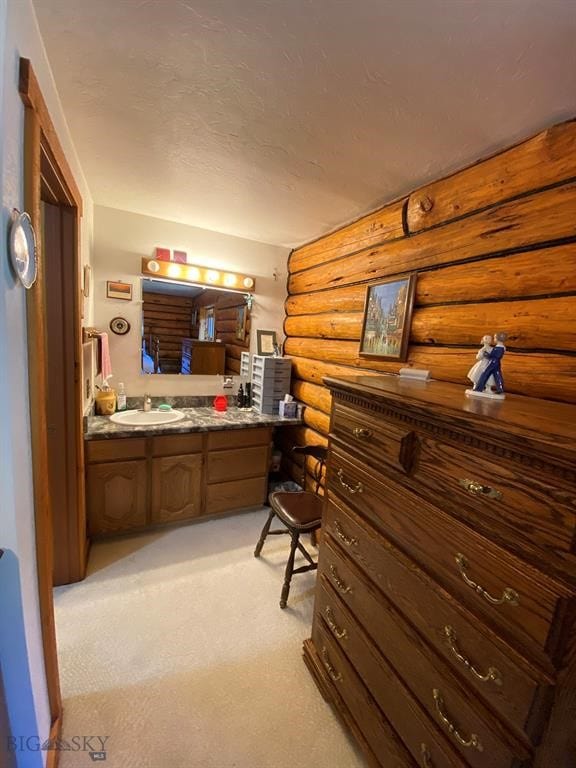 interior space featuring light colored carpet, ensuite bathroom, rustic walls, and sink