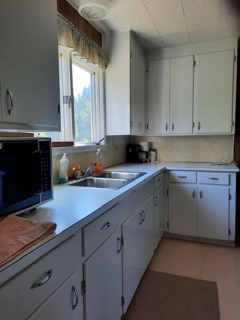 kitchen featuring tasteful backsplash, white cabinetry, sink, and light tile patterned floors