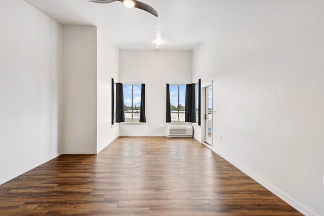 unfurnished room with an AC wall unit, ceiling fan, dark hardwood / wood-style flooring, and a towering ceiling