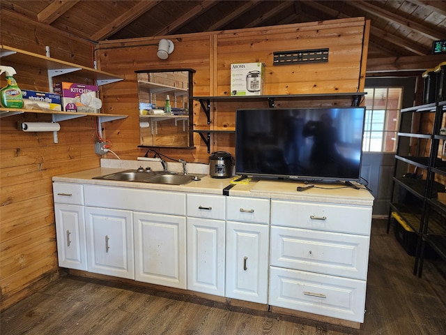 kitchen featuring sink, vaulted ceiling with beams, wooden walls, white cabinets, and wooden ceiling