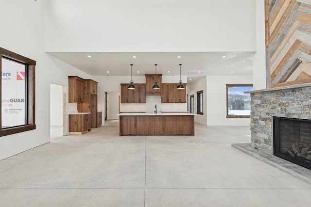 kitchen featuring decorative light fixtures, a stone fireplace, a spacious island, and a high ceiling