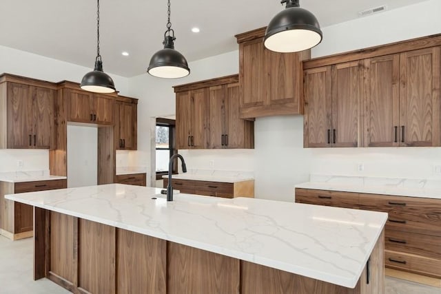 kitchen with decorative light fixtures, light stone countertops, and a kitchen island with sink