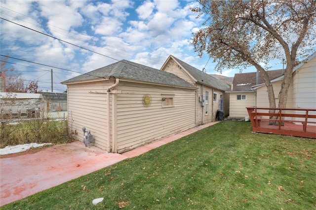 back of property with a deck, a patio, a shingled roof, and a yard