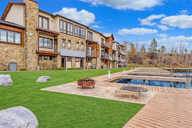 rear view of property featuring a lawn, cooling unit, and a fire pit