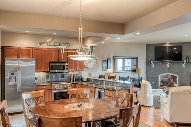 kitchen with sink, tasteful backsplash, hanging light fixtures, dark stone countertops, and appliances with stainless steel finishes