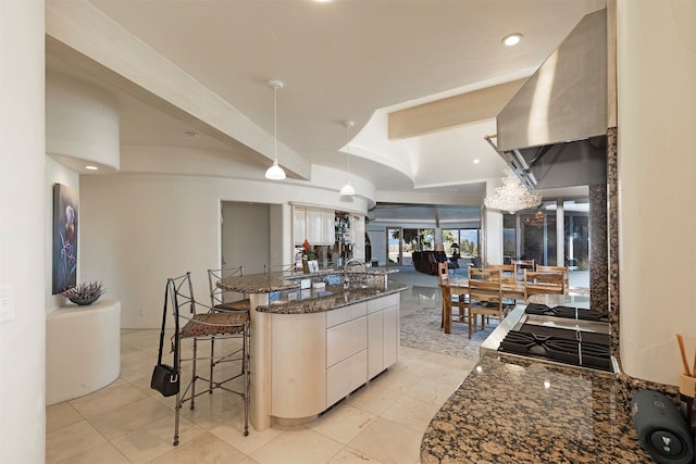 kitchen featuring a kitchen bar, hanging light fixtures, beamed ceiling, dark stone counters, and white cabinets