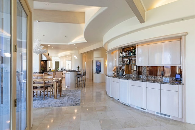 kitchen featuring kitchen peninsula, range hood, dark stone countertops, pendant lighting, and white cabinets