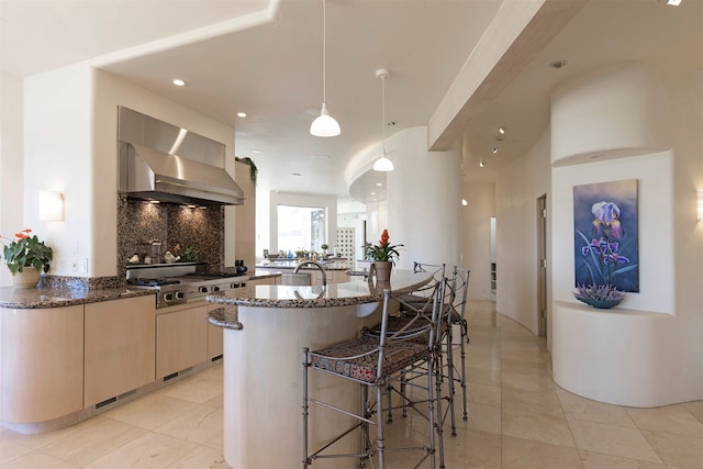 kitchen featuring decorative backsplash, hanging light fixtures, a kitchen breakfast bar, dark stone counters, and wall chimney exhaust hood