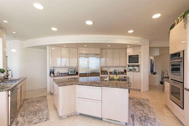 kitchen with a center island with sink, white cabinets, stainless steel appliances, and dark stone counters