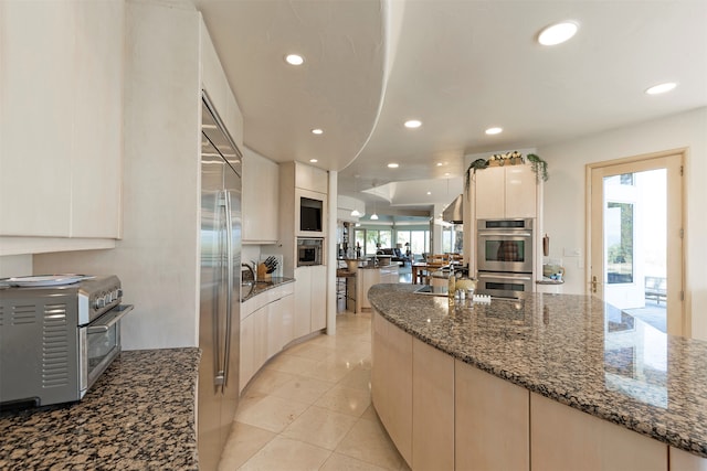 kitchen featuring dark stone countertops, stainless steel appliances, white cabinetry, and light tile patterned floors