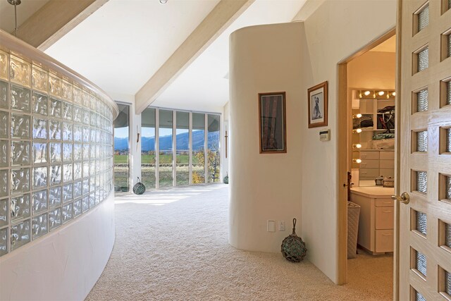 corridor with beam ceiling, a mountain view, light colored carpet, and high vaulted ceiling