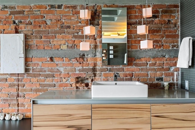 interior space with light brown cabinetry, decorative light fixtures, stainless steel counters, and sink