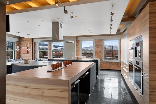 kitchen with island range hood, a kitchen island, decorative light fixtures, brick wall, and track lighting