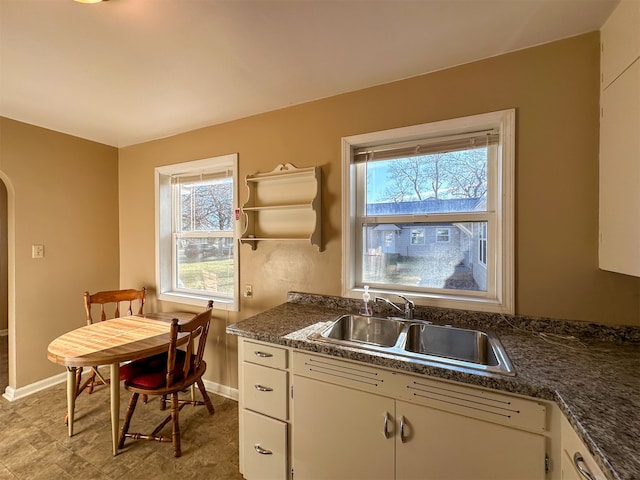 kitchen featuring dark stone counters, white cabinetry, sink, and light tile flooring