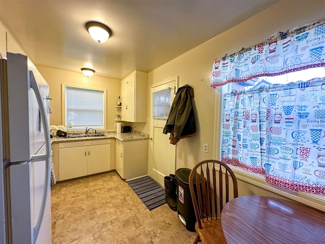 kitchen with light tile floors, light stone countertops, white cabinets, stainless steel refrigerator, and sink