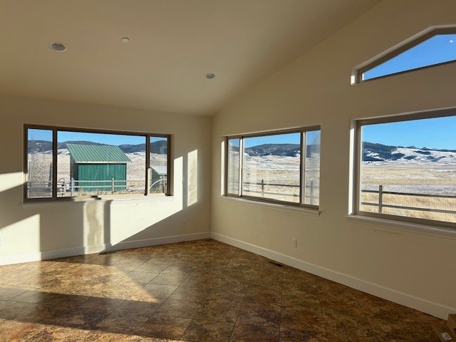 unfurnished room with lofted ceiling, dark tile flooring, and a mountain view