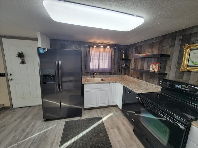 kitchen featuring white cabinets, wooden walls, light wood-type flooring, and black appliances