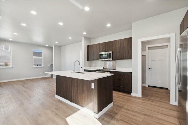 kitchen featuring dark brown cabinetry, sink, a center island with sink, and appliances with stainless steel finishes